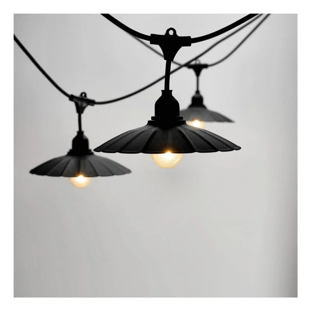 Close-up zijaanzicht van een zwarte outdoor lichtslinger met drie brandende lampen, voorzien van vintage stijl metalen kappen tegen een neutrale achtergrond.