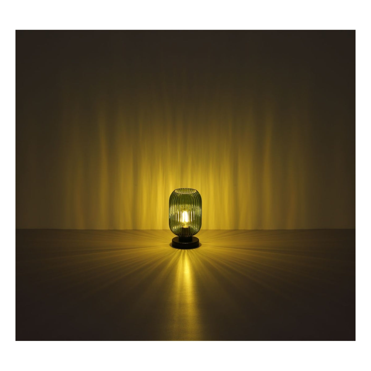Sfeervolle frontale afbeelding van de Blomus lantaarn Ani in olijfgroen, geplaatst op een tafel in een donkere ruimte met warme lichtstralen die zich rondom verspreiden.