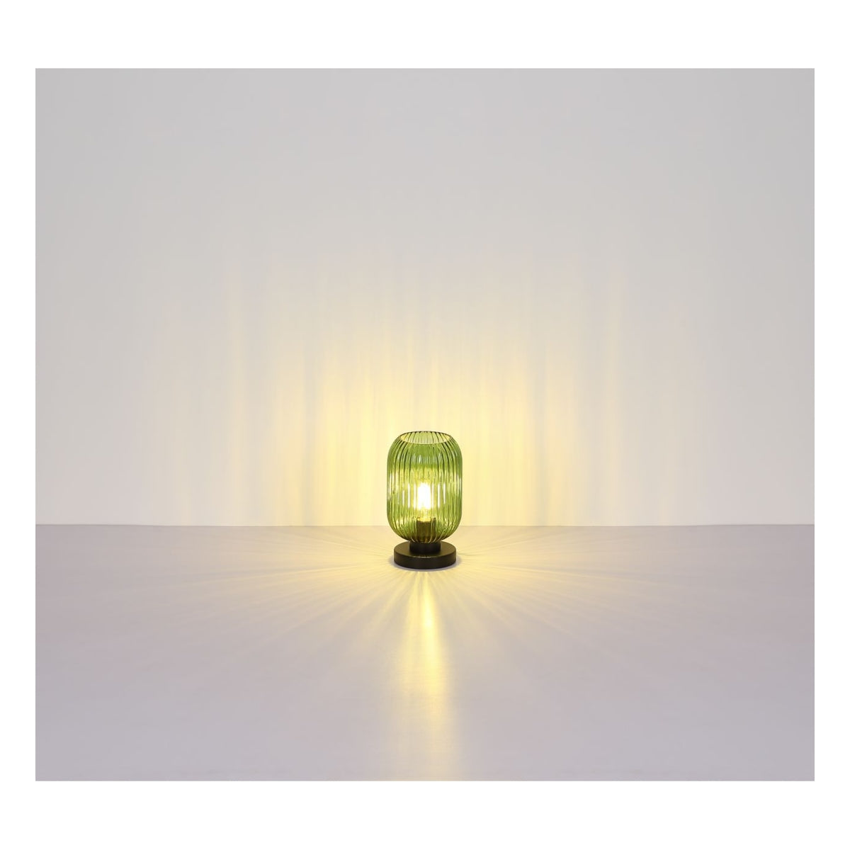Groene glazen tafellamp op zwarte voet met verticale ribbels, brandend en gecentreerd weergegeven in frontaal aanzicht tegen een neutrale achtergrond met sfeervolle lichtverspreiding.