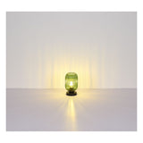 Groene glazen tafellamp op zwarte voet met verticale ribbels, brandend en gecentreerd weergegeven in frontaal aanzicht tegen een neutrale achtergrond met sfeervolle lichtverspreiding.