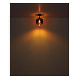 Plafondaanzicht van een brandende koperen plafondlamp met warme sfeerverlichting die een decoratief lichteffect op het plafond en muur creëert.