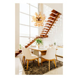 Moderne eettafelset met zes beige stoffen stoelen en een houten eettafel op een grijze vloerkleed, gezien vanuit een frontaal aanzicht in een lichte eetkamer met hoge plafonds, zwevende houten trap, grote ramen en een opvallende gouden bolvormige design hanglamp.