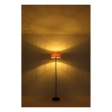 Staande lamp met industriële metalen draadkap en warme sfeerverlichting, frontaal aanzicht tegen een muur met verspreid lichtpatroon.