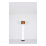 Staande lamp met zwarte metalen voet en een cilindervormige lampenkap van bruin geweven materiaal omringd door een zwart metalen rasterstructuur, frontaal aanzicht tegen een witte achtergrond.