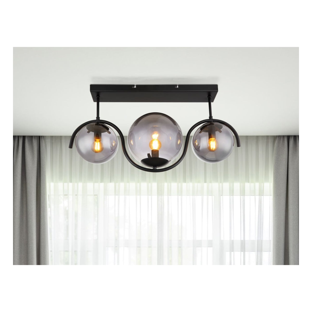 Moderne zwarte plafondlamp met drie glazen bollen en zichtbaar filament, frontaal aanzicht tegen een witte plafondachtergrond met gordijnen en natuurlijk licht.