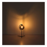 Zijaanzicht van een moderne tafellamp met ronde glazen kap en warm licht, geplaatst tegen een neutrale achtergrond voor een sfeervolle verlichting.