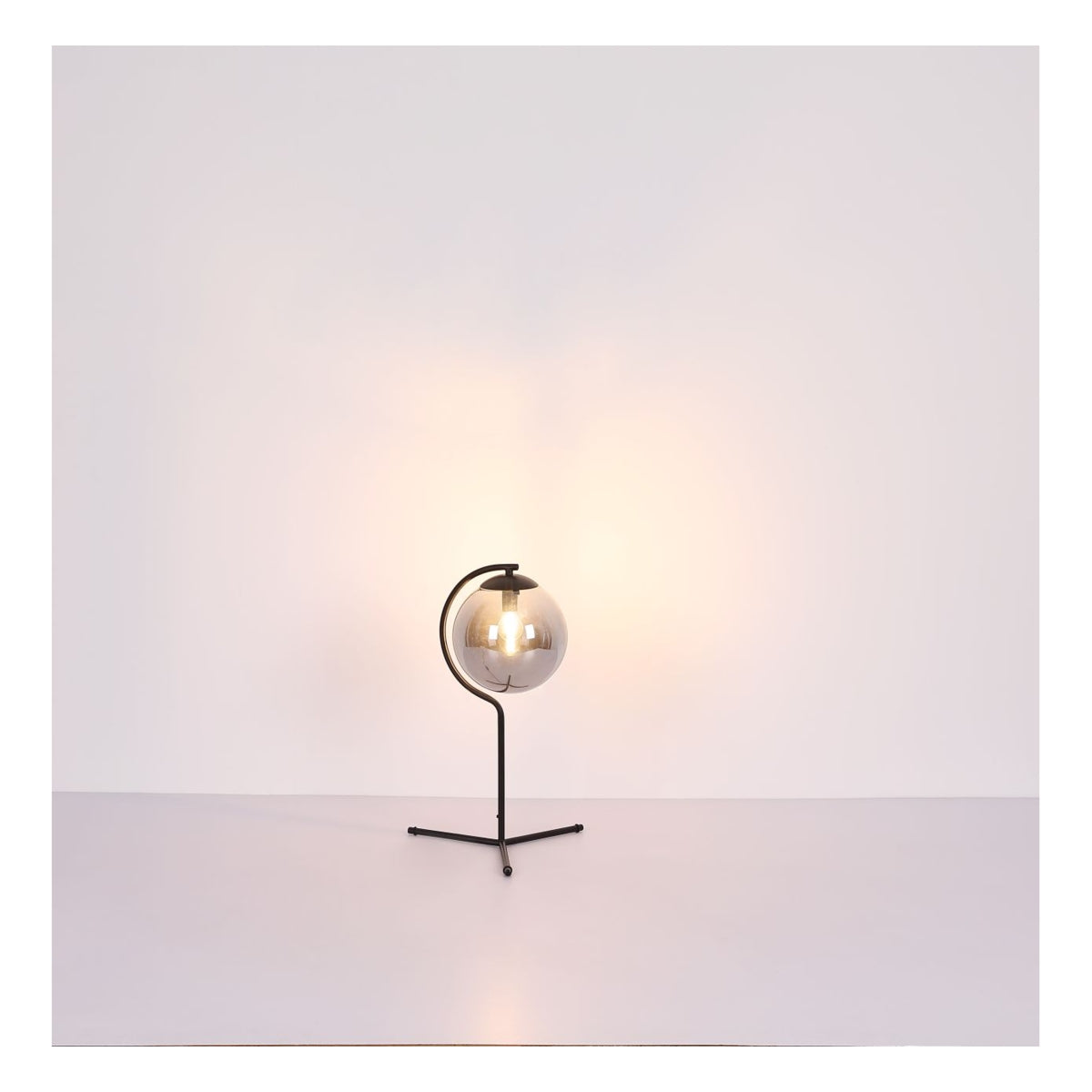 Moderne tafellamp met ronde glazen kap en zwart metalen frame, sfeervol verlicht, vooraanzicht tegen een minimalistische witte achtergrond.