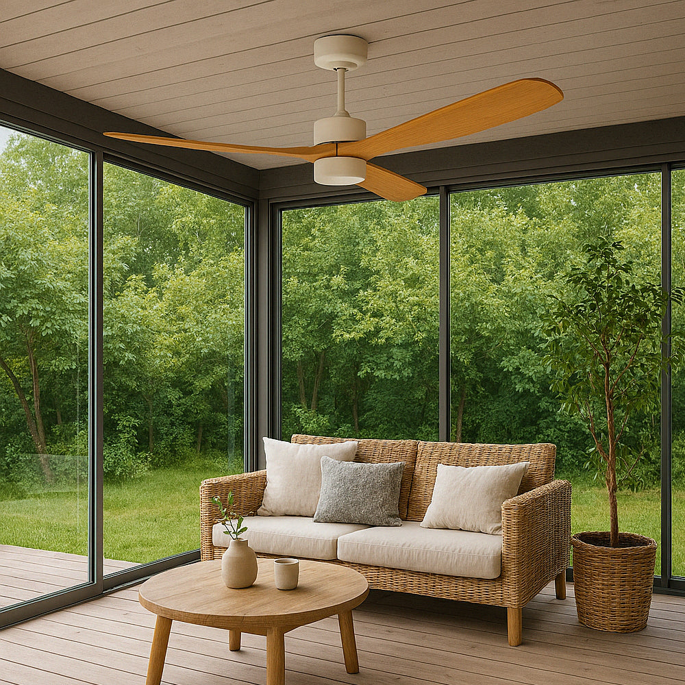 Moderne plafondventilator met houten bladen in een veranda met uitzicht op een groene tuin, gefotografeerd in vooraanzicht vanuit een lichte zithoek met rotanbank, salontafel en kamerplant.