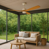 Moderne plafondventilator met houten bladen in een veranda met uitzicht op een groene tuin, gefotografeerd in vooraanzicht vanuit een lichte zithoek met rotanbank, salontafel en kamerplant.
