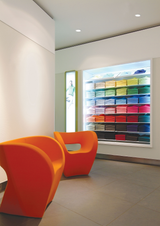 Moderne winkelinrichting met feloranje design fauteuils op de voorgrond en een kleurrijk wandrek met opgevouwen kleding op de achtergrond, frontaal aanzicht.