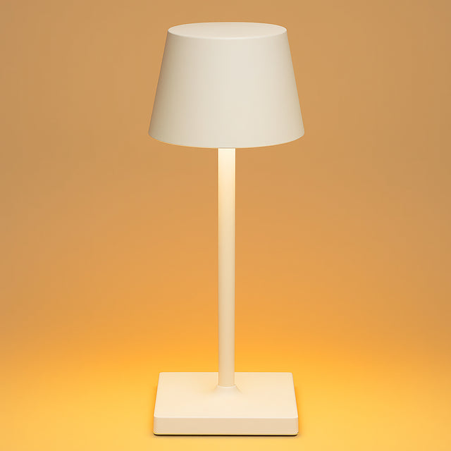 Minimalistische moderne tafellamp in een matte crèmekleurige afwerking, met een slanke verticale standaard en een kegelvormige kap, gefotografeerd van voren tegen een warm oranje achtergrond.