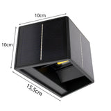 Zwart kubusvormig solar wandlampje met afmetingen 10x10x15,5 cm, schuin vanonder gefotografeerd, met zicht op het zonnepaneel aan de bovenkant en zijkanten.