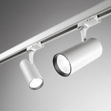 Moderne witte cilindervormige railspotverlichting gemonteerd aan een plafondrailsysteem, schuin van onderen gefotografeerd met zicht op de lampkoppen en bevestiging.