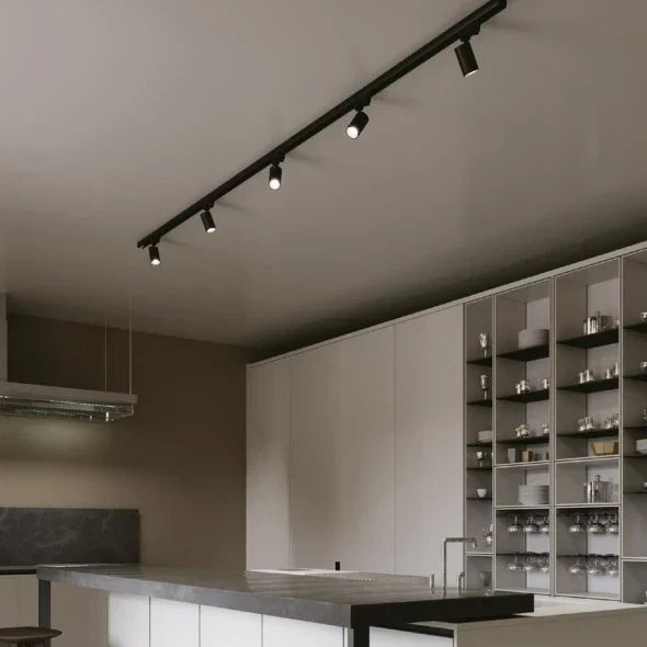 Zwarte railverlichting met vier verstelbare spotjes gemonteerd aan het plafond in een moderne keuken, vooraanzicht onder een hoek, met zicht op het kookeiland en ingebouwde kastenwand.