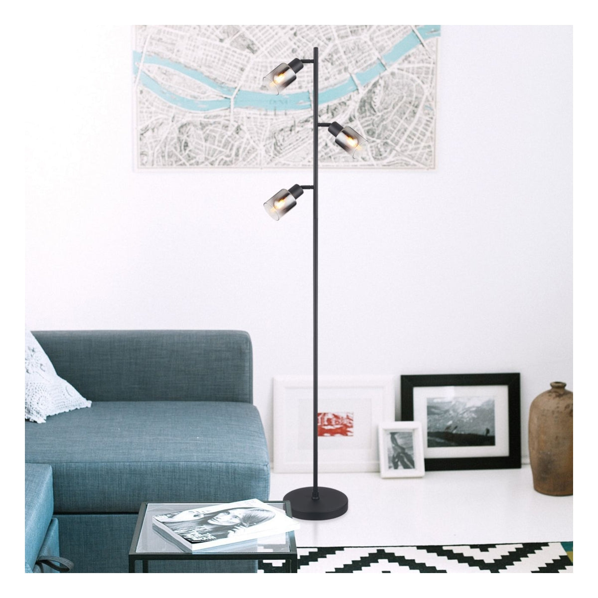 Zwarte industriële vloerlamp met drie verstelbare spots, geplaatst in een moderne woonkamer met een blauwe bank en wanddecoratie, vooraanzicht.