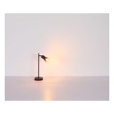 Moderne zwarte tafellamp met glazen kap en warme verlichting, zijaanzicht tegen een minimalistische witte achtergrond.