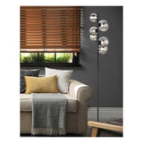 Moderne staande lamp met zes ronde glazen bollen op zwarte metalen standaard, geplaatst naast een beige bank in een stijlvolle woonkamer – zijaanzicht met focus op het product in zijn interieurcontext.