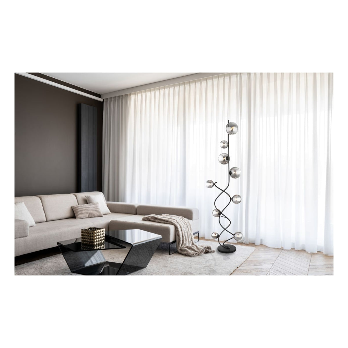 Staande designlamp met meerdere rookglas bollen en zwart metalen frame, vooraanzicht, geplaatst in een moderne woonkamer met lichtinval door witte gordijnen.