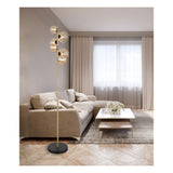 Moderne staande lamp met goudkleurige metalen staander en zes glazen bollen als lampenkappen, geplaatst in een elegant en neutraal ingerichte woonkamer met beige bank, lichte gordijnen en een houten salontafel – frontaal aanzicht.