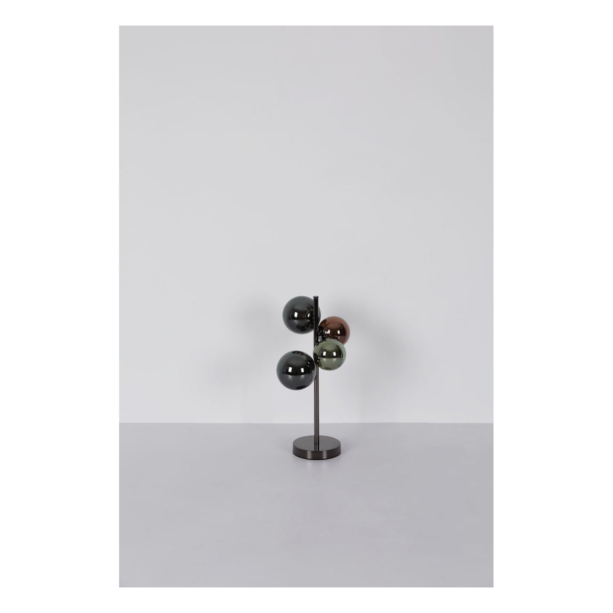 Moderne meerkleurige tafellamp met vier glanzende bolvormige lampenkappen op een verticale metalen standaard, gefotografeerd van voren tegen een neutrale achtergrond.