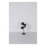 Moderne meerkleurige tafellamp met vier glanzende bolvormige lampenkappen op een verticale metalen standaard, gefotografeerd van voren tegen een neutrale achtergrond.