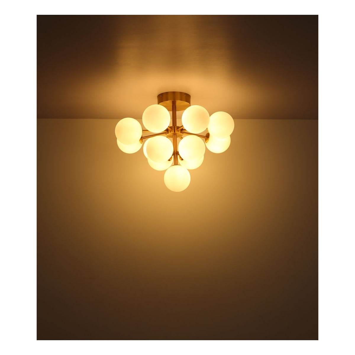 Moderne plafondlamp met 12 ronde melkglazen bollen en messingkleurige armaturen, gezien vanaf de onderzijde in een verlichte omgeving tegen een lichtgekleurde plafond- en wandachtergrond.