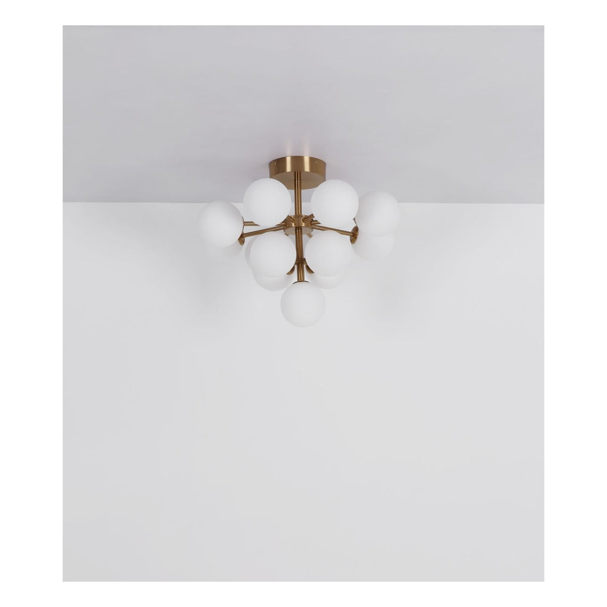 Moderne plafondlamp met matgouden armatuur en meerdere ronde, witte opaalglazen bollen, gefotografeerd in frontaal aanzicht tegen een witte plafond- en wandachtergrond.