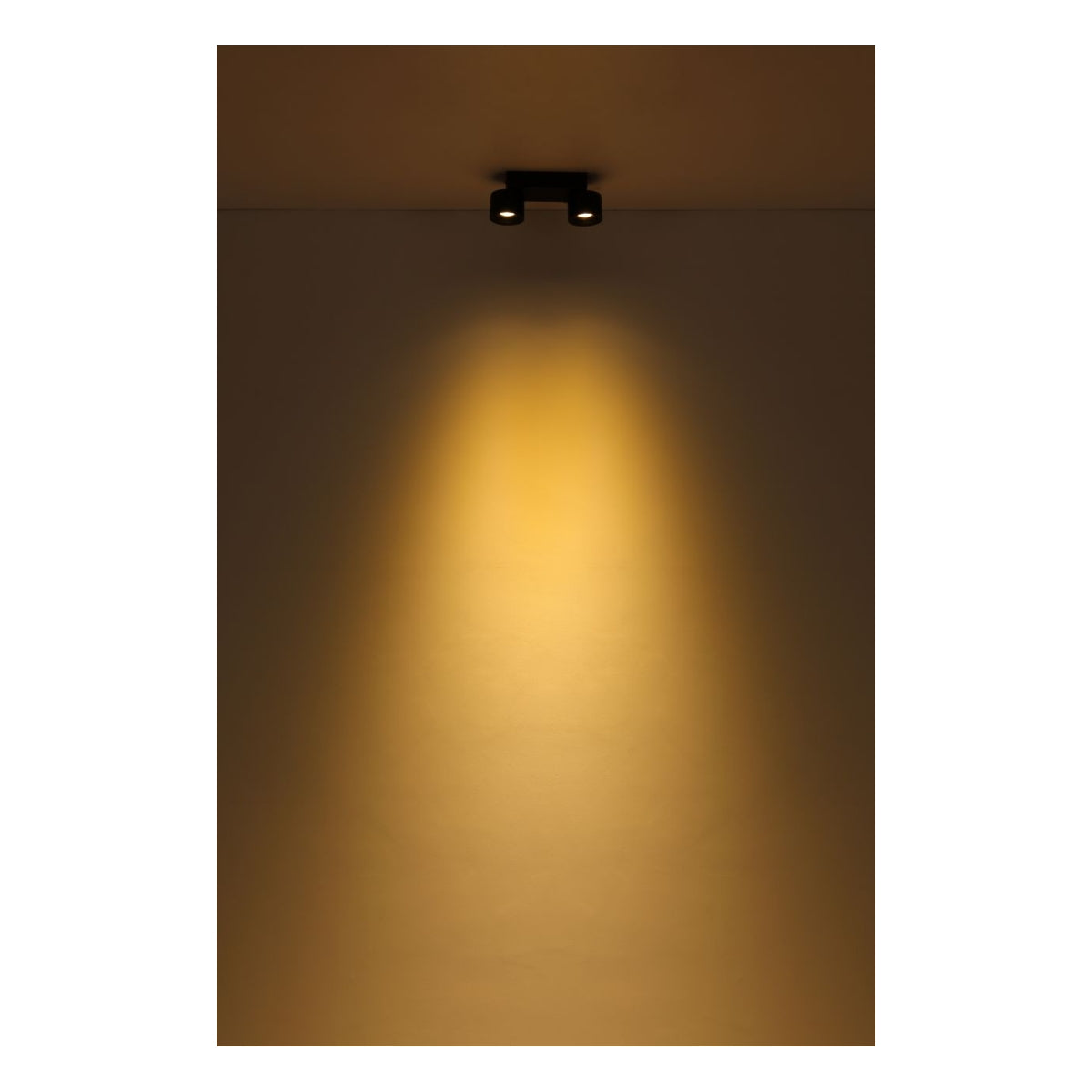 Zwarte dubbele opbouwspot aan plafond in werking, met warm wit licht gericht naar beneden op muur – vooraanzicht van moderne plafondverlichting in donkere ruimte.