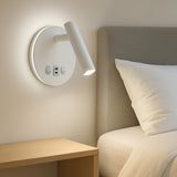 Witte moderne wandlamp met USB-poort en bedieningsknoppen, gemonteerd naast een bed met lichtgrijze hoofdbord en houten nachtkastje, gefotografeerd in zijaanzicht in een slaapkameromgeving.