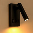 Zijaanzicht van een moderne zwarte wandlamp met verstelbare cilindervormige spot, ingebouwde schakelaar en stopcontact, gemonteerd op een beige muur en met warm wit licht.
