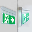 Dubbelzijdig verlichte nooduitgang bewegwijzering met groene achtergrond en witte pictogrammen van een rennend persoon en pijl naar rechts, gemonteerd aan een muurhoek, schuinaanzicht.