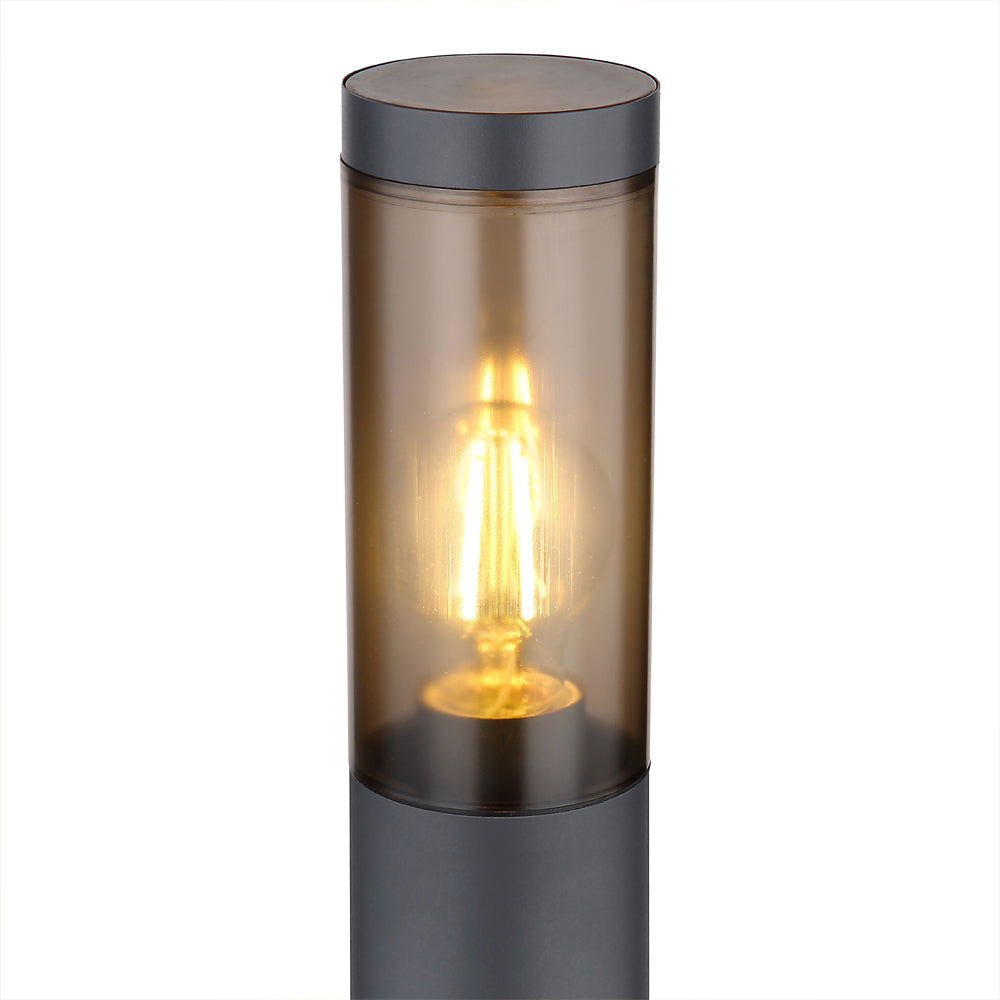 Close-up zijaanzicht van een moderne buitenlamp met een cilindervormig ontwerp, zwarte behuizing en warm amberkleurig glas, waarin een brandende LED filamentlamp zichtbaar is.