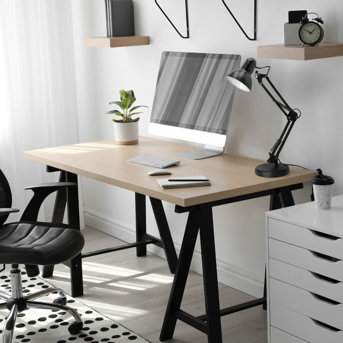 Moderne thuiswerkplek met een licht houten bureau met zwarte schragen, voorzien van een computer, bureaulamp, notitieboekje en plant, gefotografeerd in een zijaanzicht met daglichtinval vanaf links.