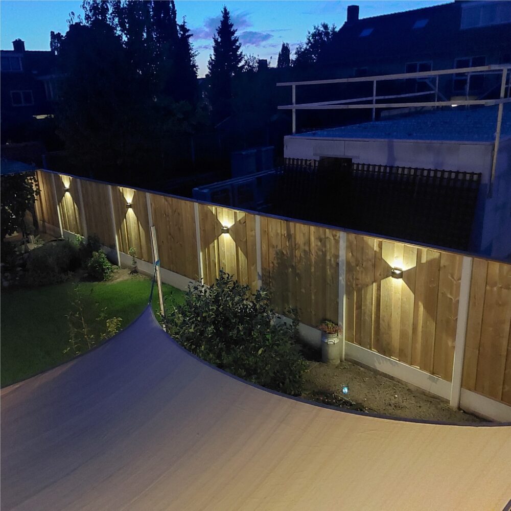 Houten schutting verlicht met moderne wandlampen op zonne-energie in een sfeervol verlichte achtertuin tijdens de schemering, zijaanzicht.