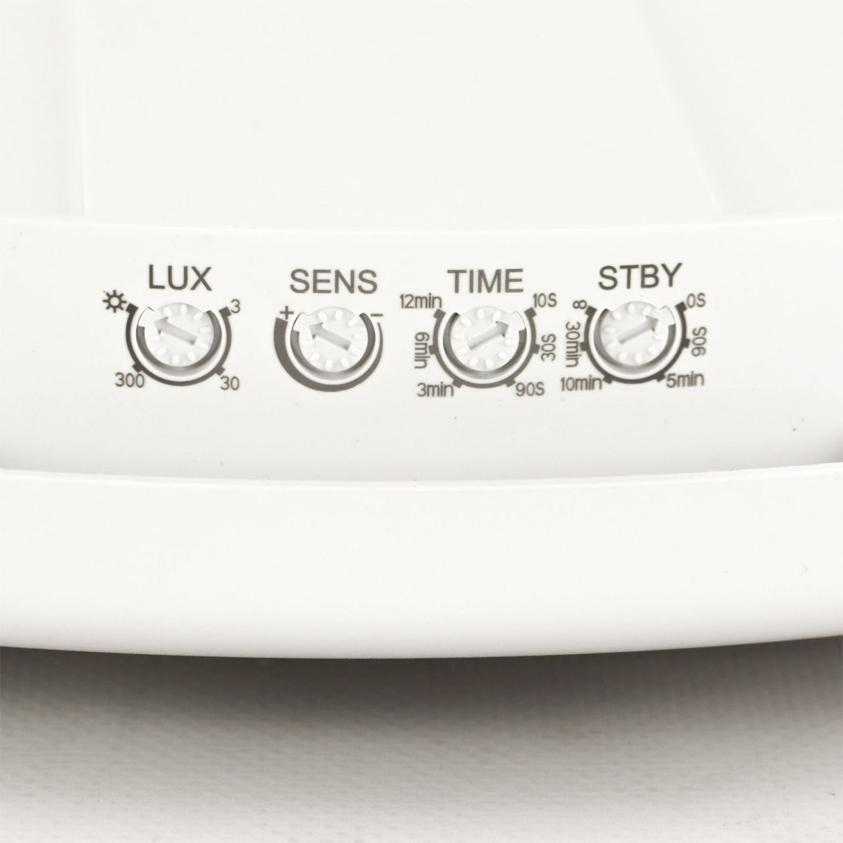 Close-up van de bedieningsknoppen op een witte bewegingssensorlamp, met zicht op de instelbare draaiknoppen voor LUX, SENS, TIME en STBY aan de voorkant.