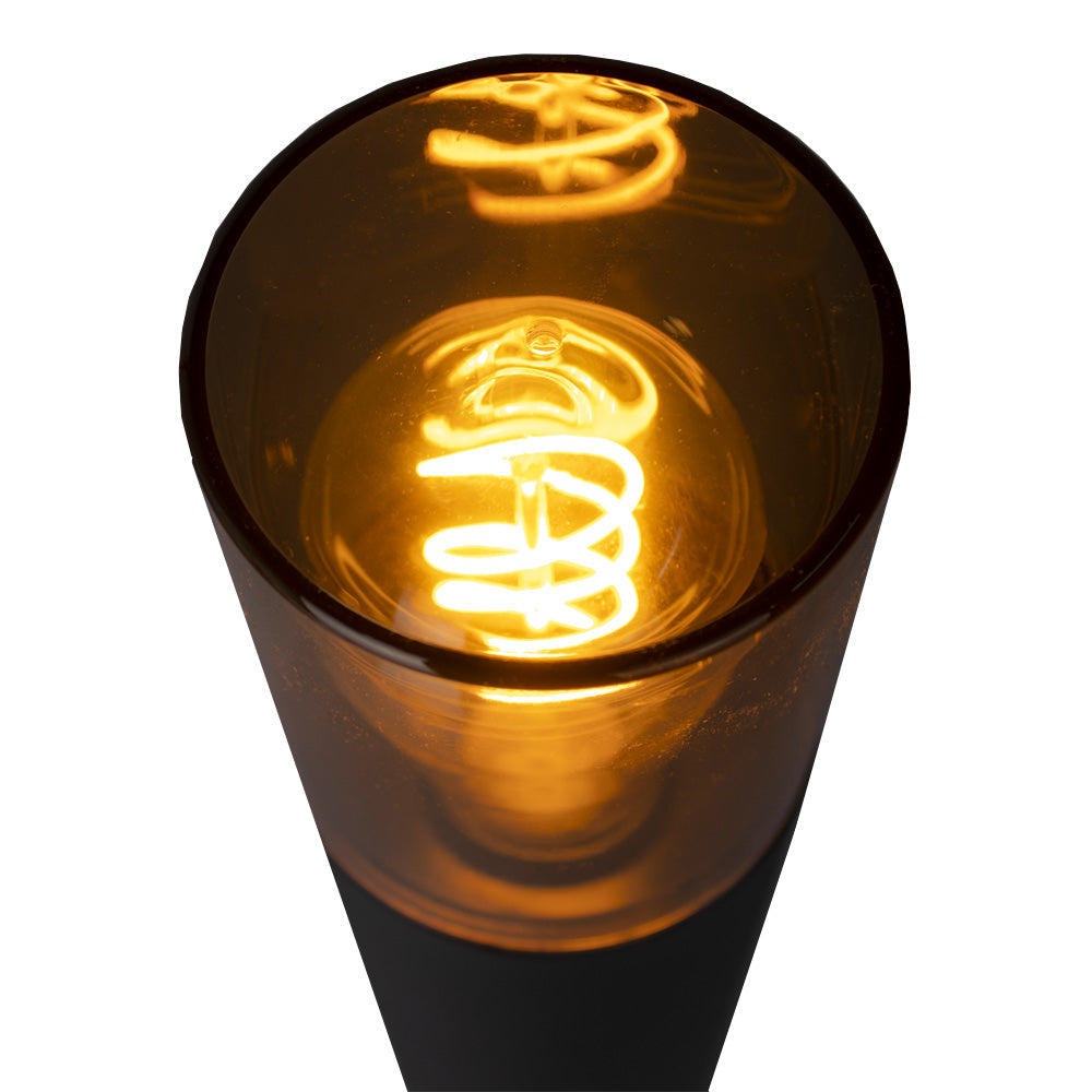 Close-up bovenaanzicht van een moderne tafellamp met een spiraalvormige LED filament lichtbron in een amberkleurige glazen kap, die warm geel licht uitstraalt.