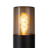 Close-up van een moderne tafellamp met spiraalvormige LED filament, zichtbaar door een cilindervormige, getinte glazen kap op een matzwarte basis, vooraanzicht.