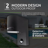 Moderne zwarte buitenlamp met sensor en geïntegreerde lichtbron, zijaanzicht tegen een onscherpe achtergrond van een tuin met zwembad; voorzien van een detectieafstand tot 8 meter en geschikt voor directe aansluiting op het stroomnet.