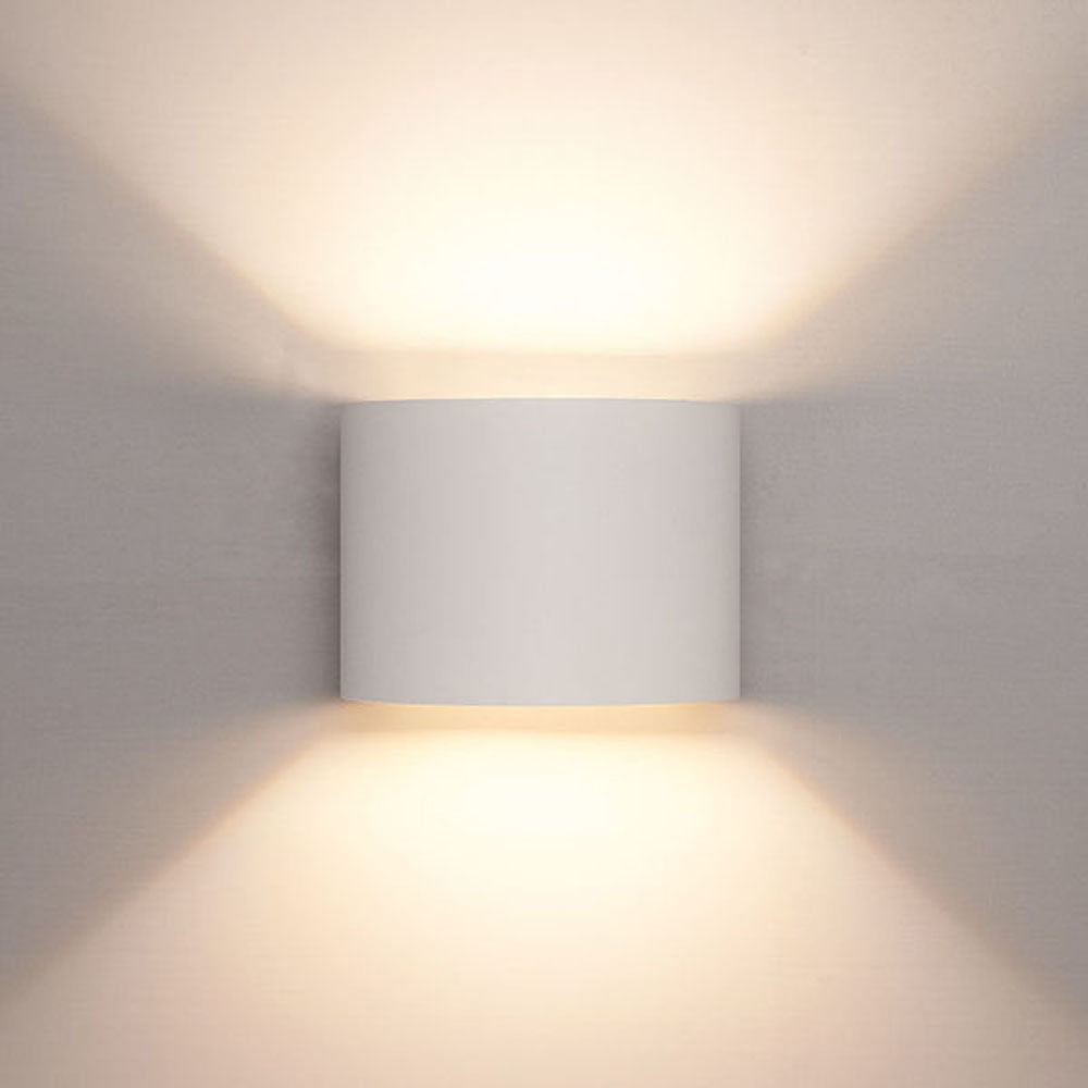Moderne witte wandlamp met cilindervormig ontwerp, straalt warm licht naar boven en beneden uit, frontaal aanzicht tegen een neutrale muur.