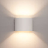 Moderne witte wandlamp met cilindervormig ontwerp, straalt warm licht naar boven en beneden uit, frontaal aanzicht tegen een neutrale muur.