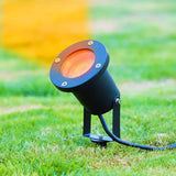 Buiten LED grondsportlamp met oranje lichtstraal, zijaanzicht op grasveld, geschikt voor tuinverlichting en sfeerverlichting.