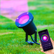 Zwarte slimme RGB LED-buitenspot op gras, met roze lichtstraal, bediend via smartphone-app – zijaanzicht.