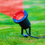 Zwarte LED buitenspot met rood licht straalt schuin naar boven, geplaatst op een grasveld – zijaanzicht van het armatuur met zichtbaar aansluitingssnoer.
