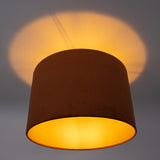 Cilindervormige plafondlamp met fluwelen kap in warme oranje gloed, gezien van schuin onderaanzicht met indirect lichtschijnsel op het plafond.