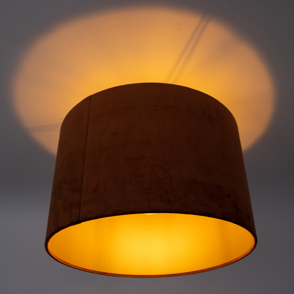 Close-up onderaanzicht van een ronde plafondlamp met een donkerbruine stoffen kap en warme binnenverlichting, die een sfeervolle lichtcirkel op het plafond projecteert.