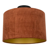 Ronde plafondlamp met fluwelen lampenkap in roestbruine kleur en gouden binnenzijde, frontaal schuin van onderen gefotografeerd.