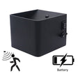 Zwarte vierkante wandlamp met bewegingssensor en batterijvoeding, schuin vooraanzicht met zicht op aan/uit schakelaar en instelknop aan de zijkant.