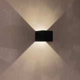 Moderne zwarte wandlamp met op- en neerwaartse lichtbundels, gemonteerd op een decoratief gestucte muur – vooraanzicht.