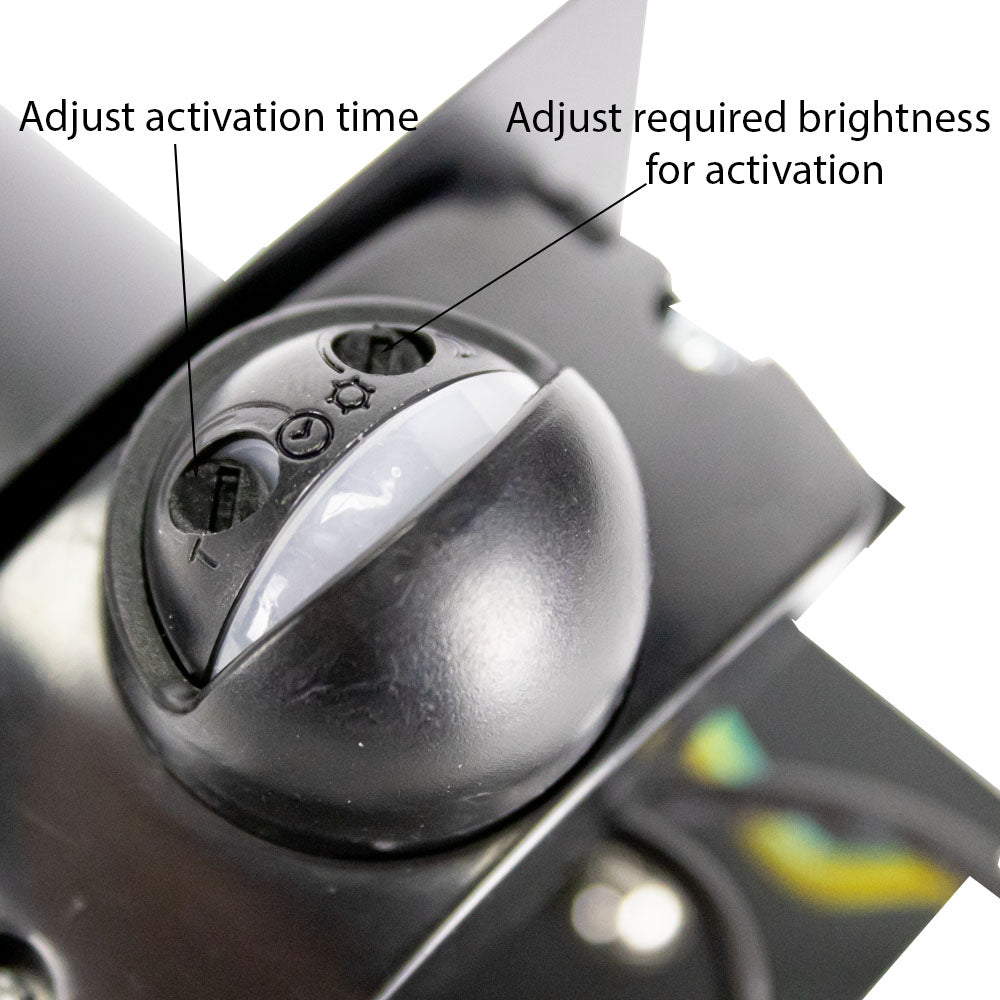 Close-up van een bewegingssensor met instelbare draaiknoppen voor activatieduur en lichtgevoeligheid, gemonteerd op een zwart metalen oppervlak, schuine bovenaanzicht.