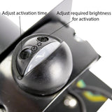 Close-up van een bewegingssensor met instelbare draaiknoppen voor activatieduur en lichtgevoeligheid, gemonteerd op een zwart metalen oppervlak, schuine bovenaanzicht.